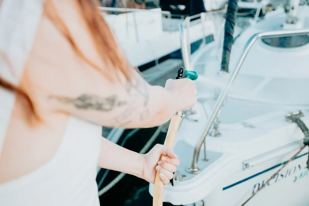 A young cheerful woman cleaning a classic sailing yacht with sweet water after sailing i
